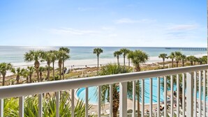 A balcony with a view of a beach, palm trees, and a pier. - Grand Panama Beach Resort by Book That Condo (Panama City Beach)