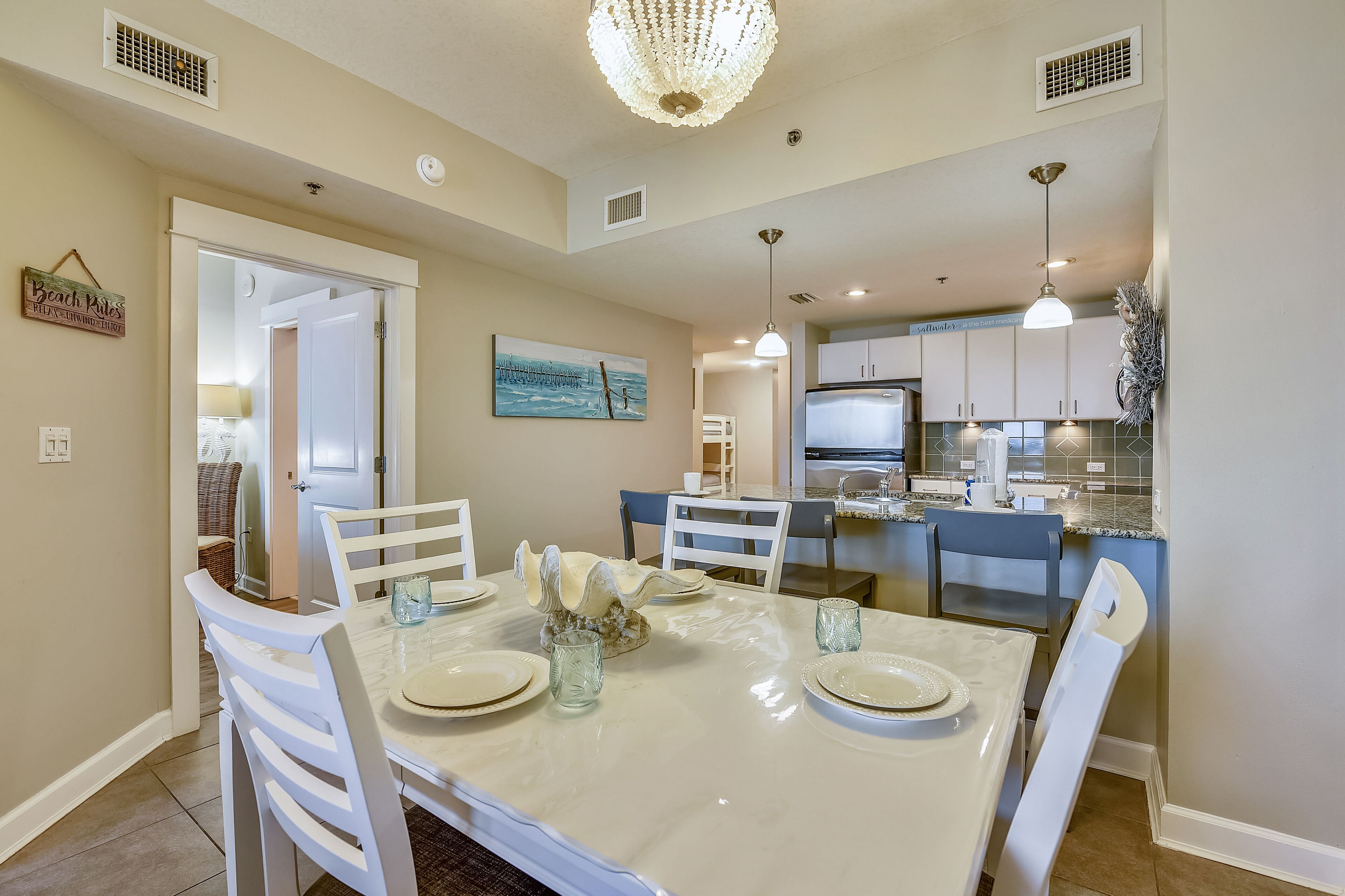 A dining area with a white table set for four, white chairs, and a chandelier.