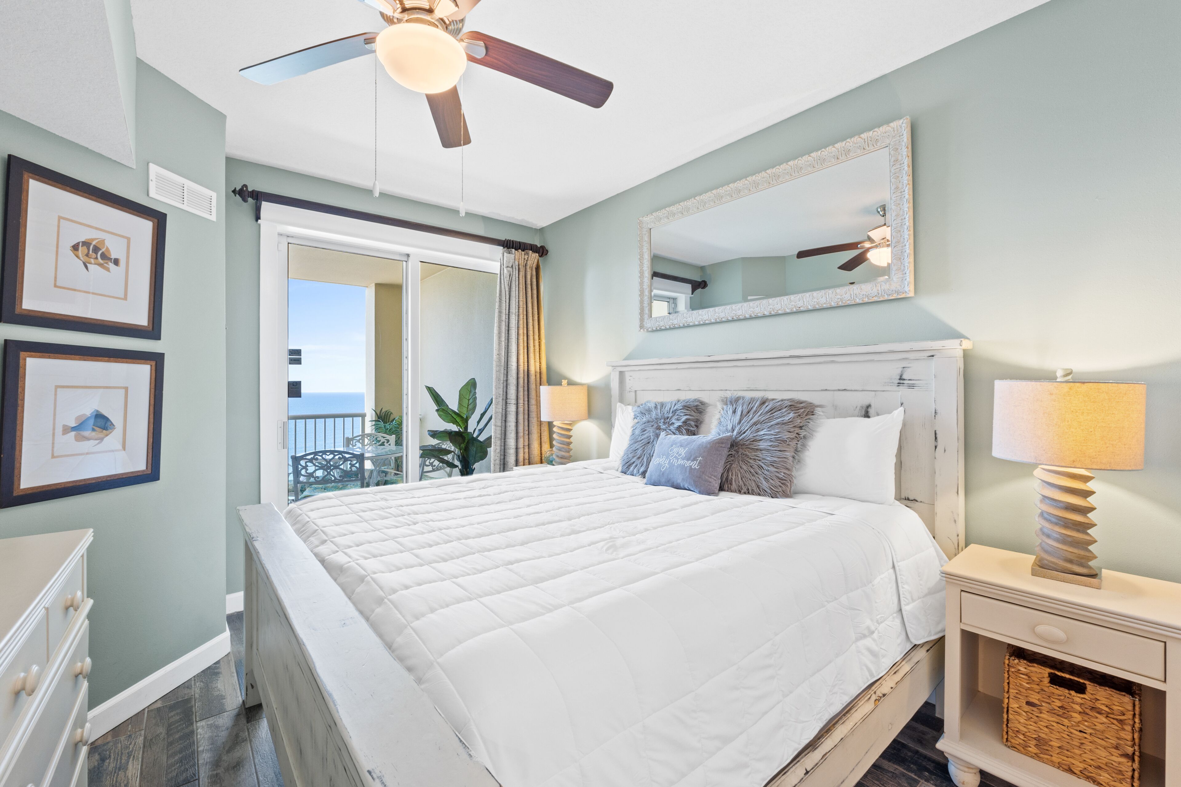 A bedroom with a bed, ceiling fan, dresser, and a view of the outdoors.