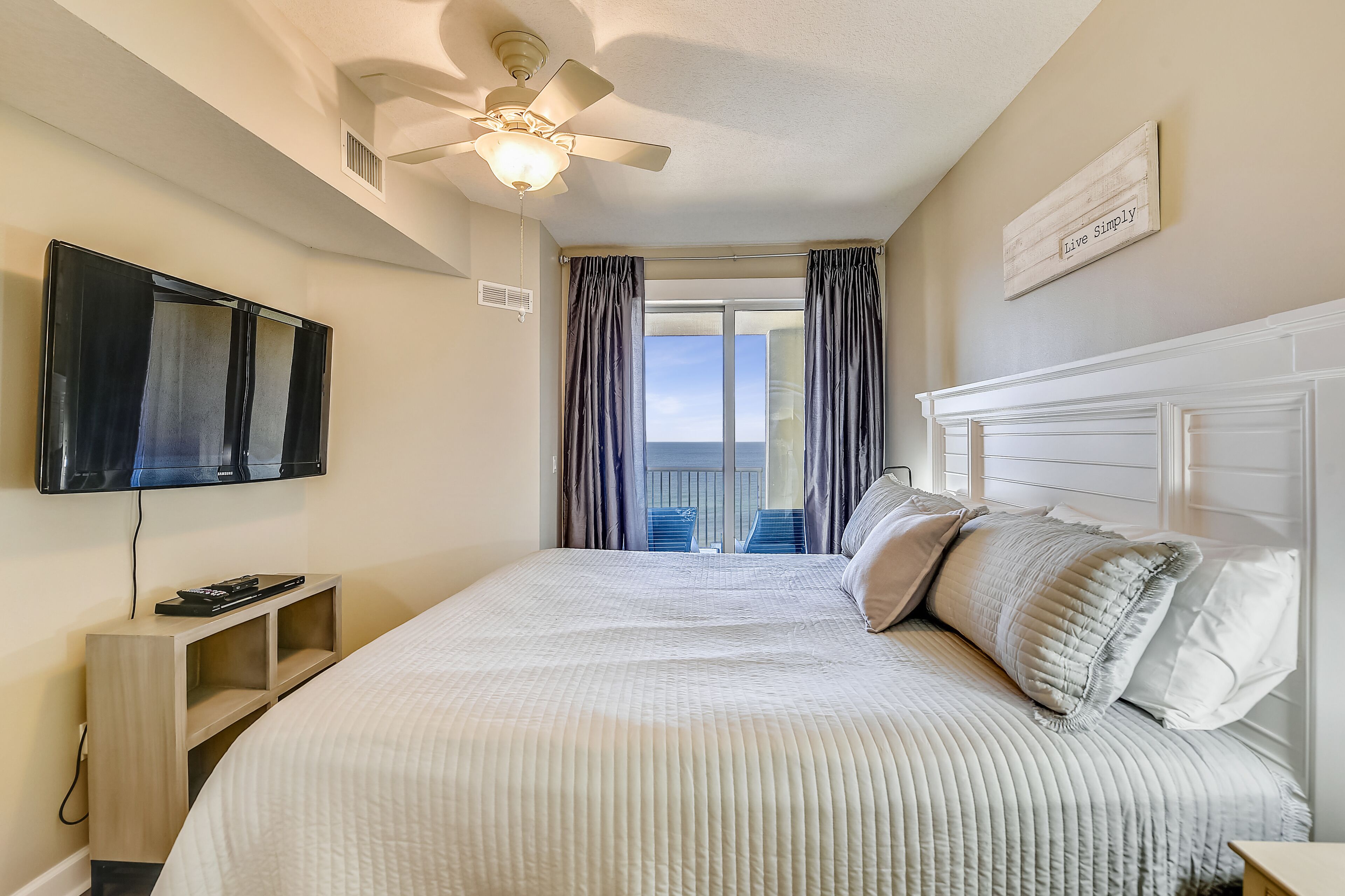 Une chambre à coucher avec un lit, un ventilateur de plafond, une télévision et une vue sur l’extérieur.