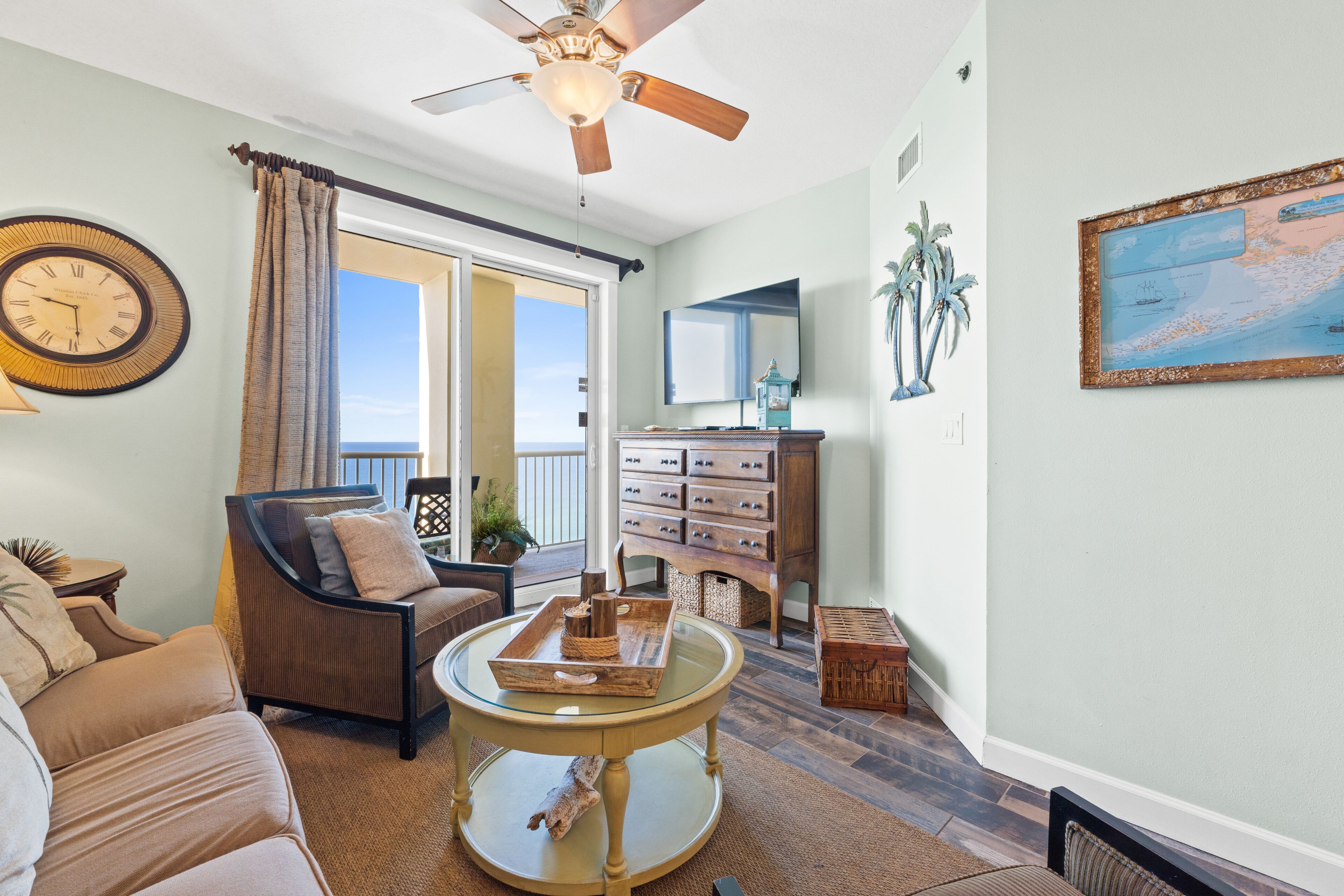 A living room with a ceiling fan, a large window with curtains, a wooden cabinet, and a framed map on the wall.
