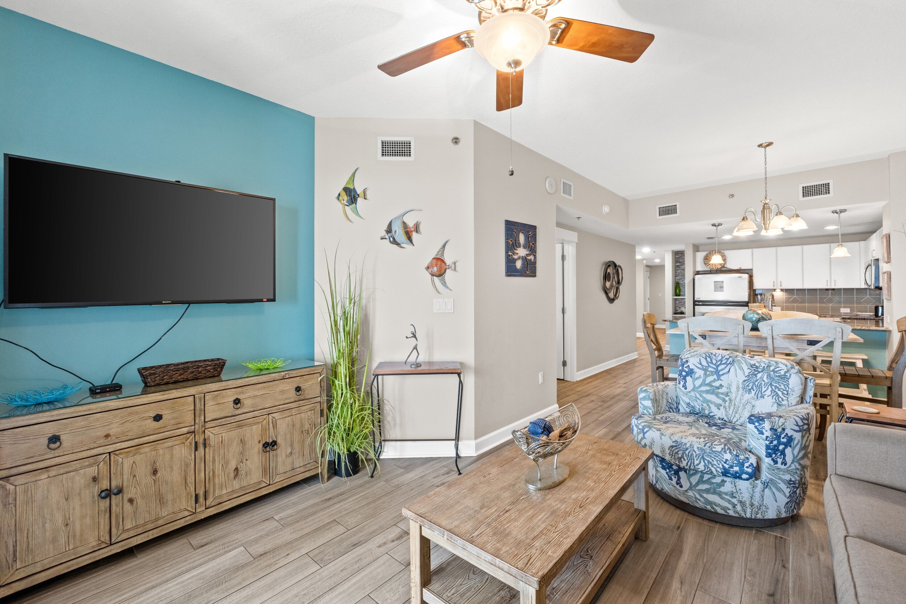 A spacious living room with a flat-screen TV, wooden furniture, and a ceiling fan.
