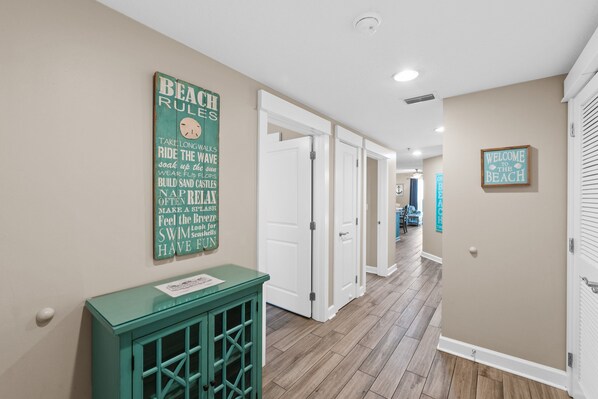 A hallway with a wooden floor, white doors, and a green cabinet. There are signs on the wall with text and a welcome sign. - Grand Panama Beach Resort by Book That Condo (Panama City Beach)