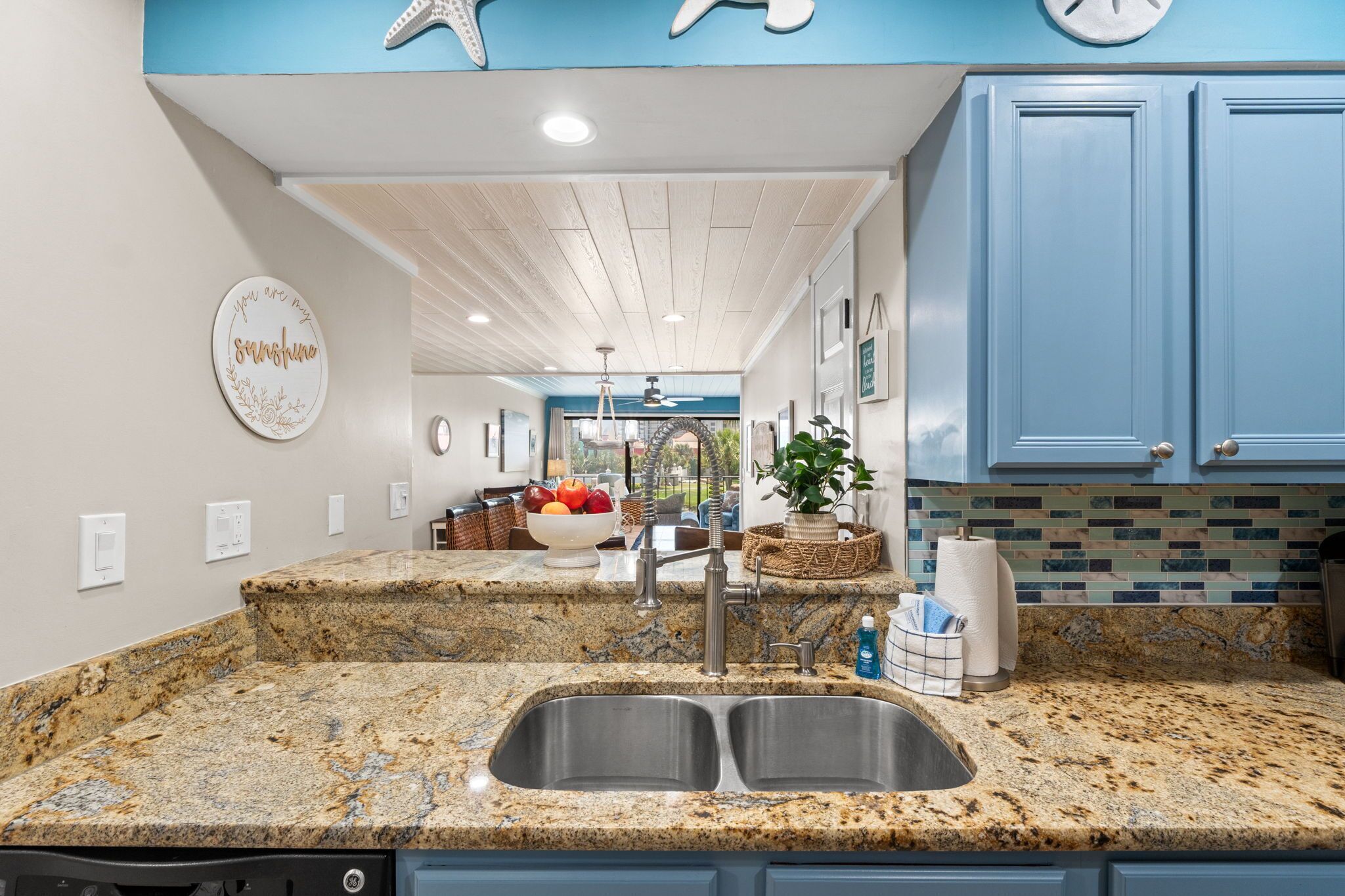 Una cocina con encimeras de granito, pileta doble, armarios azules y una decoración de estrella de mar en la pared.