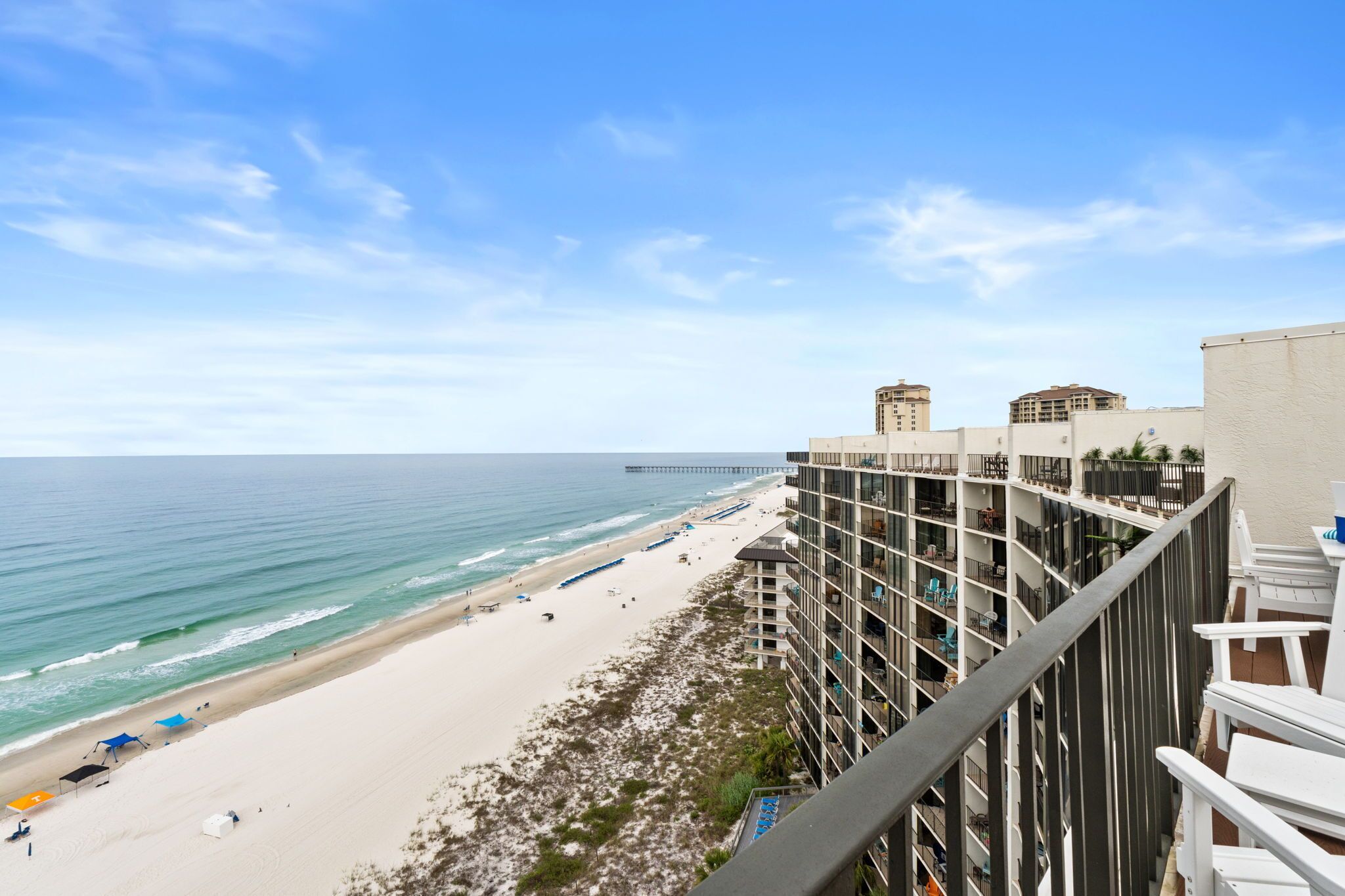 A beachfront hotel with balconies overlooking the ocean, a pier in the distance, and a sandy beach.