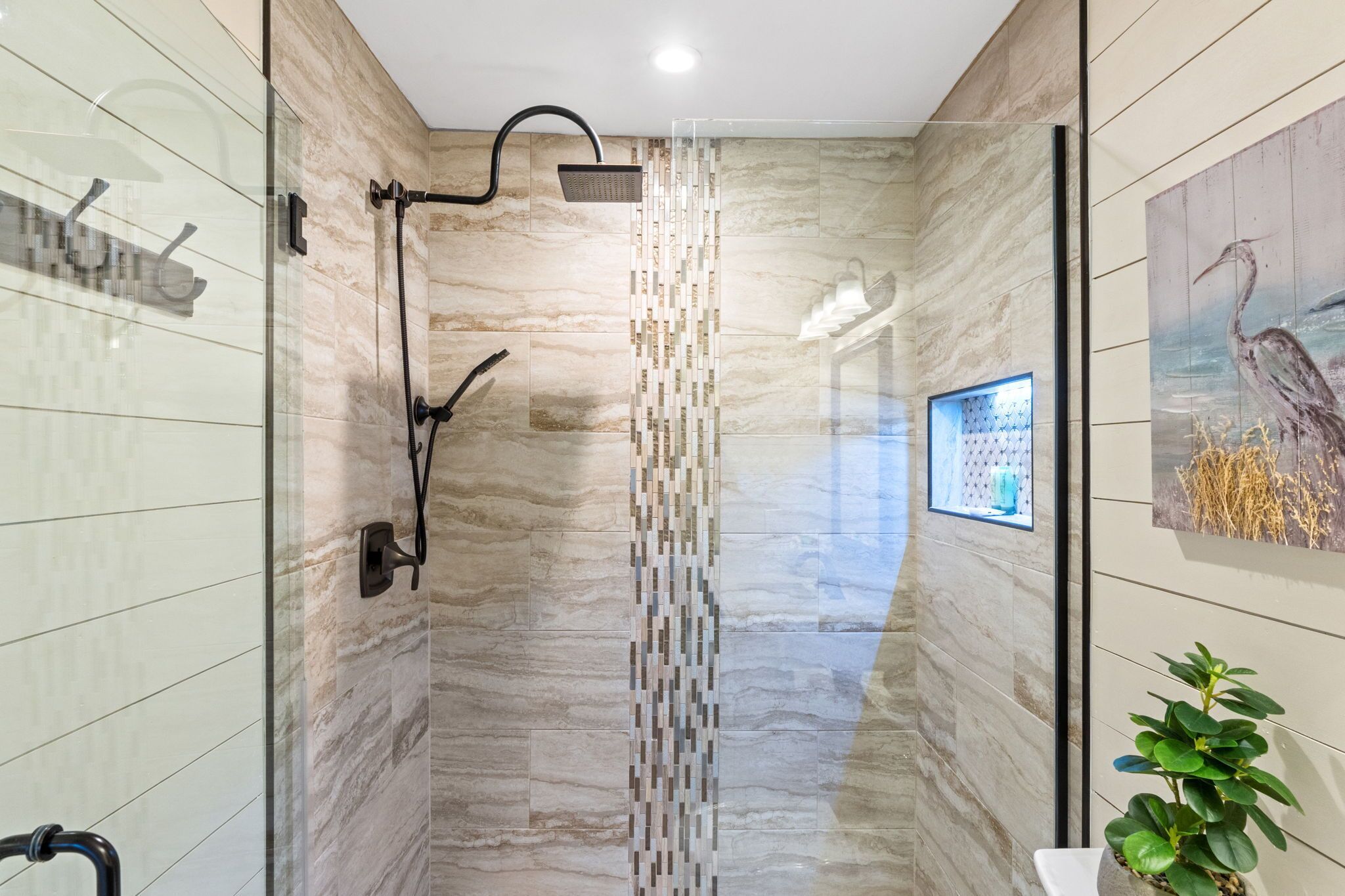 A modern bathroom with a glass shower enclosure, a vertical mosaic tile divider, and a framed artwork on the wall.