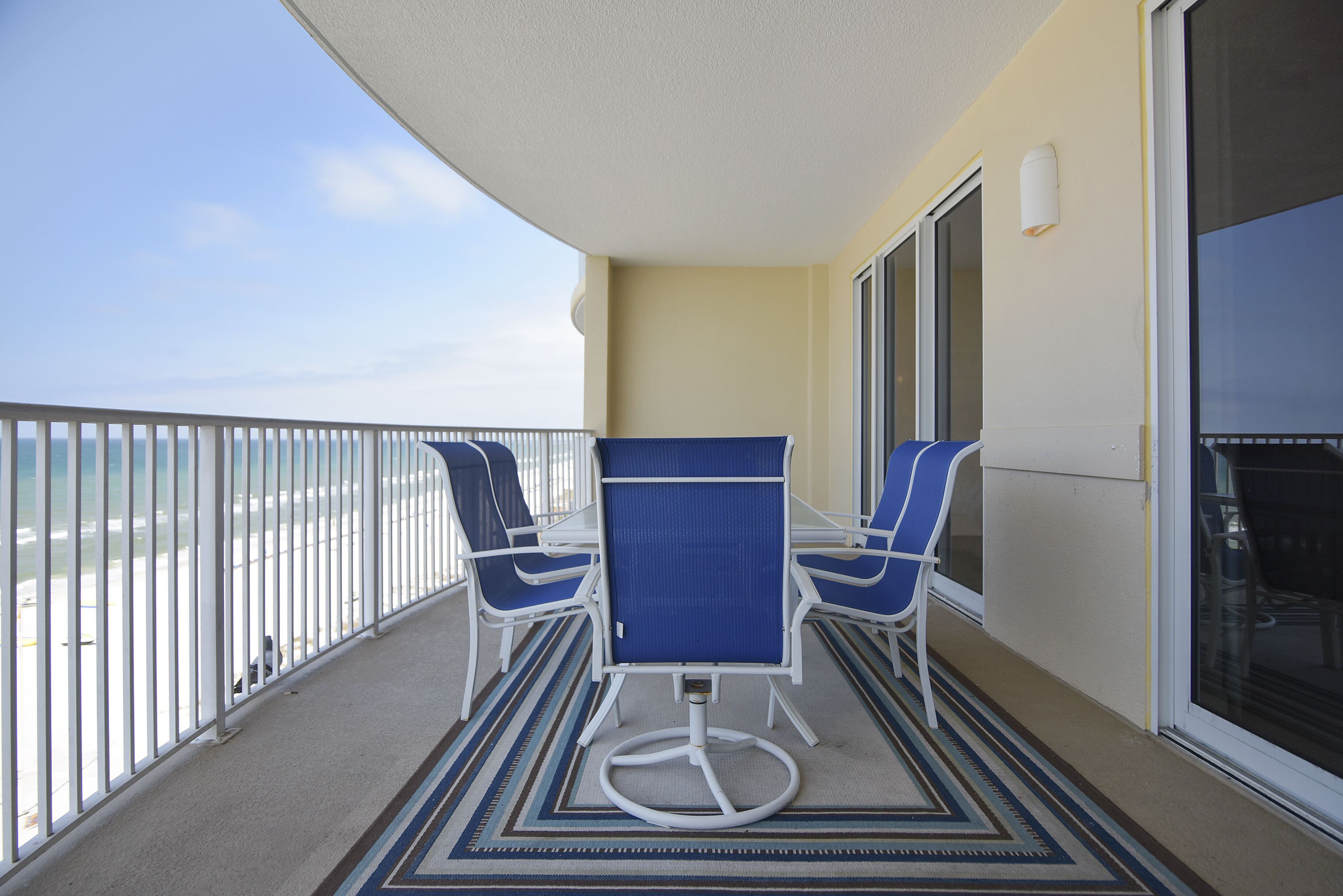 A balcony with two blue chairs and a table, overlooking a beach.