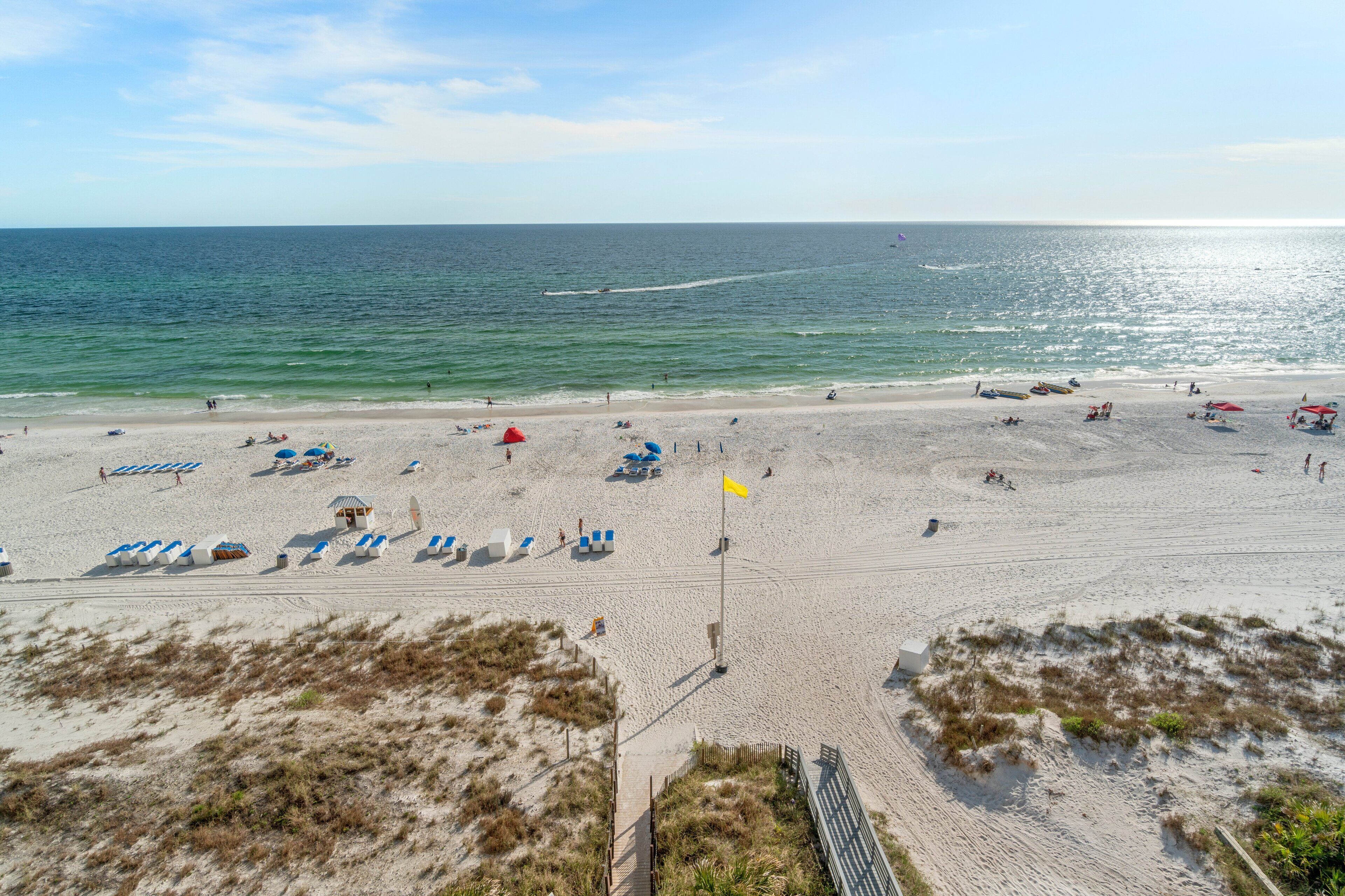 A beach with rows of beach chairs and umbrellas, a lifeguard tower, and a sandy path leading to the water.
