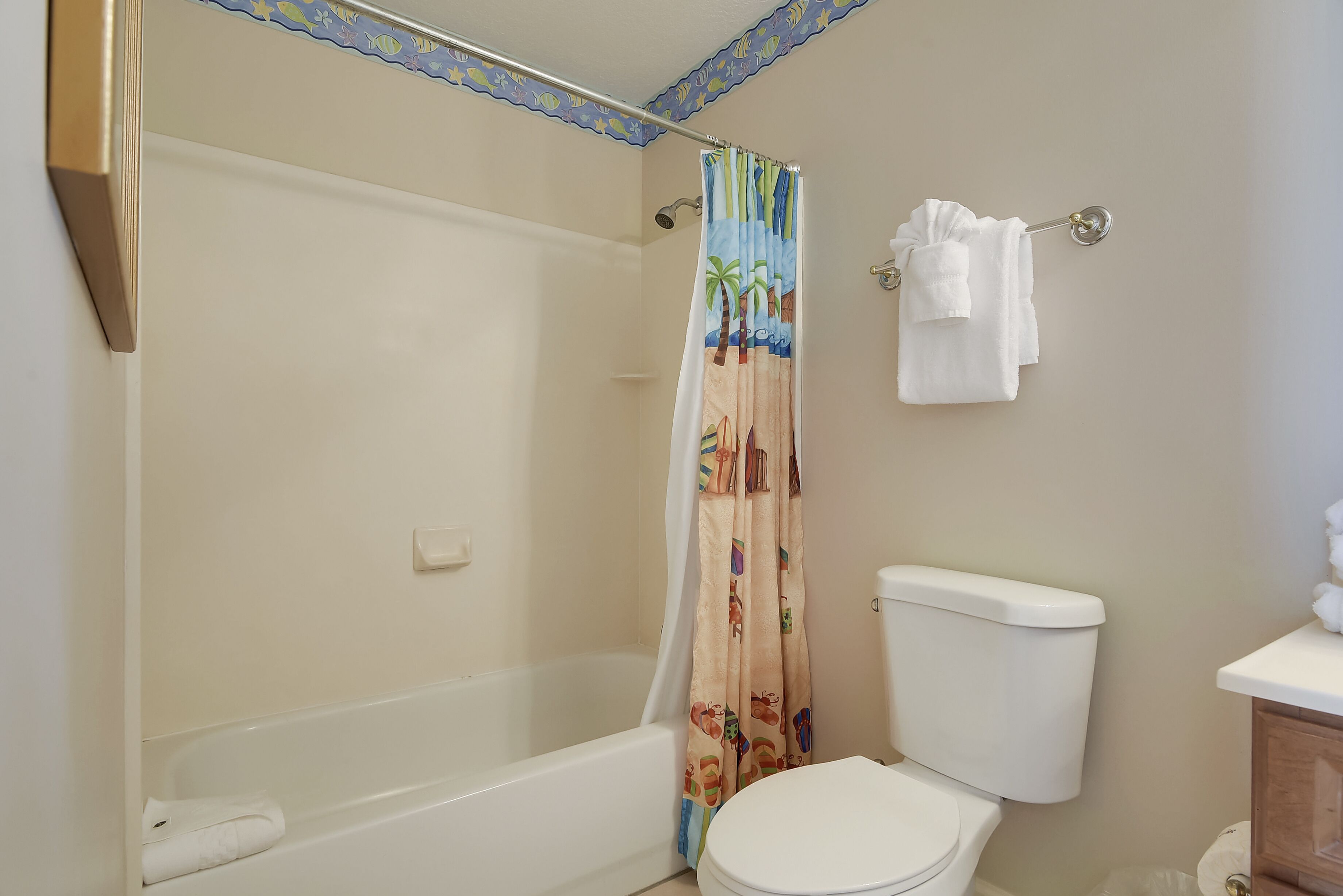 A bathroom with a bathtub, toilet, and a shower curtain with a beach theme.