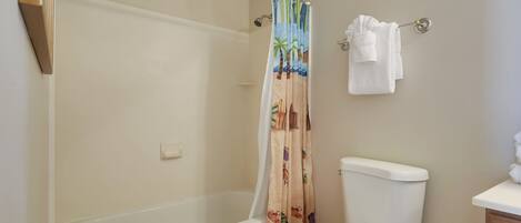 A bathroom with a bathtub, toilet, and a shower curtain with a beach theme.