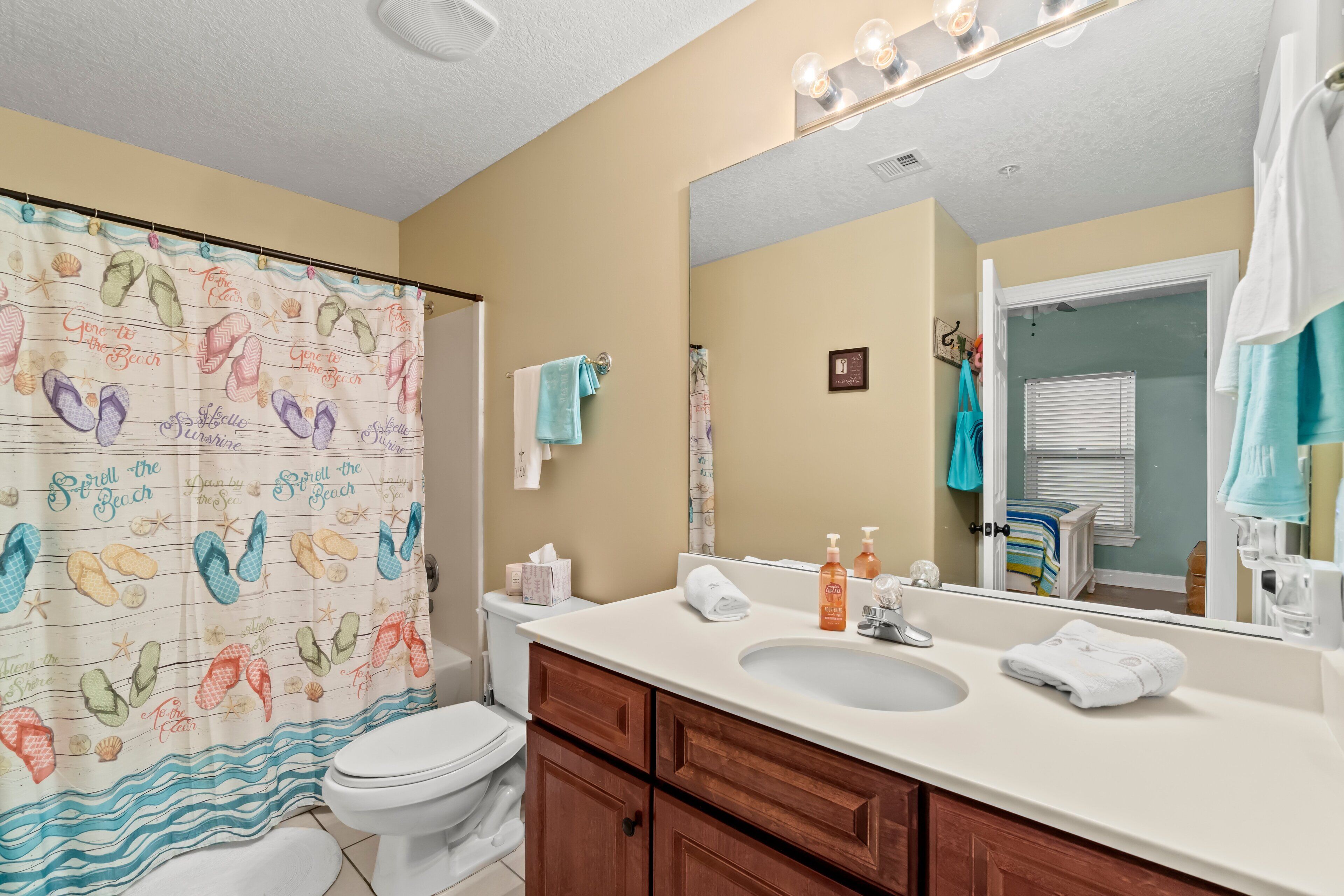A bathroom with a shower curtain featuring beach-themed designs, a sink, vanity, and a mirror.