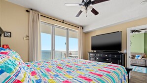 Habitación de hotel con una cama grande, televisión, ventilador de techo y balcón con vistas.
