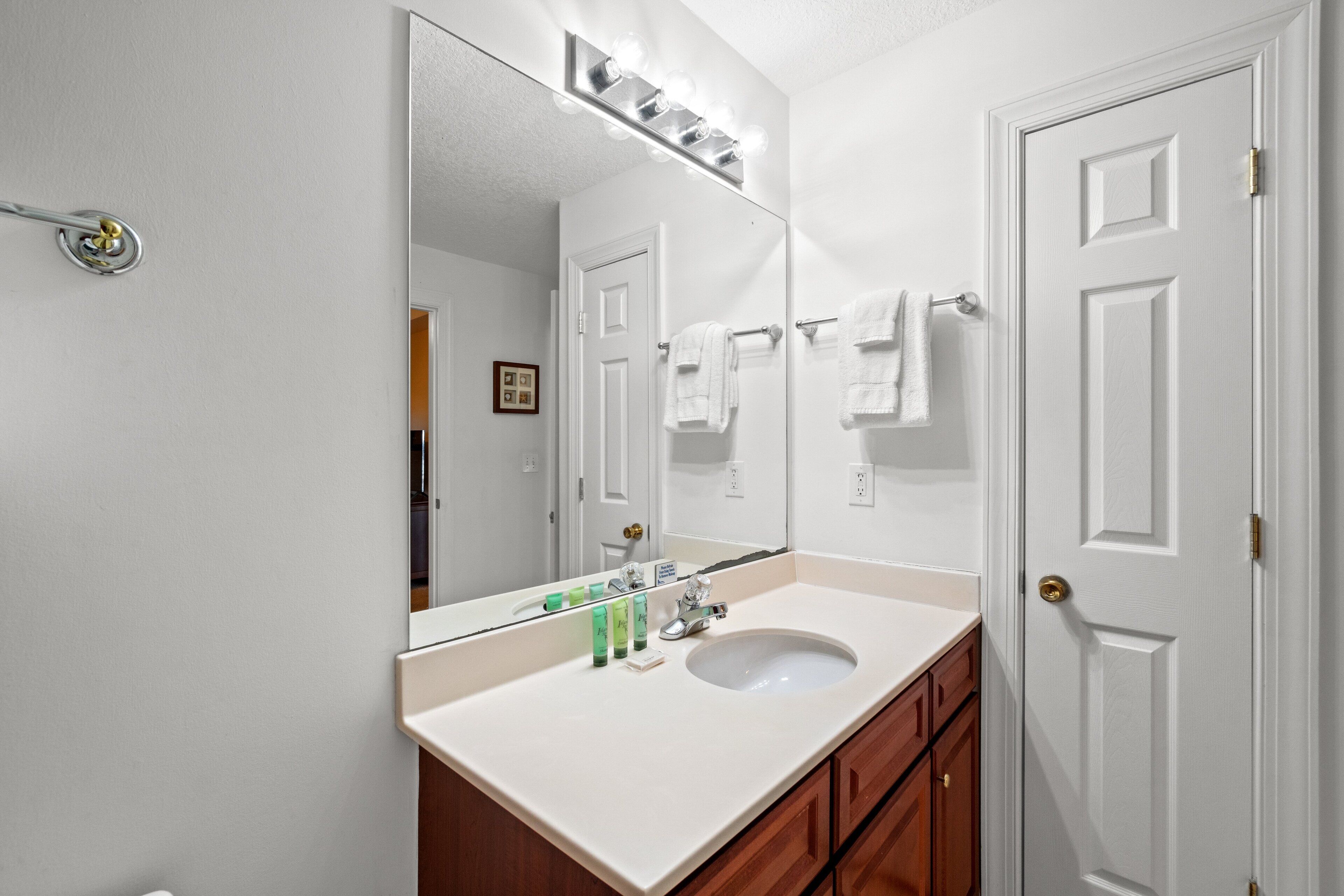 Une salle de bain avec un grand miroir, un lavabo blanc et des meubles en bois.