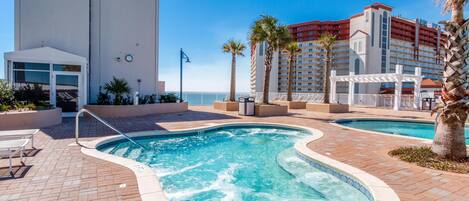 A pool area with two hot tubs, a white building, and a palm tree.