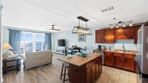 A spacious living area with a large window, a kitchen with wooden cabinets, and a dining area.
