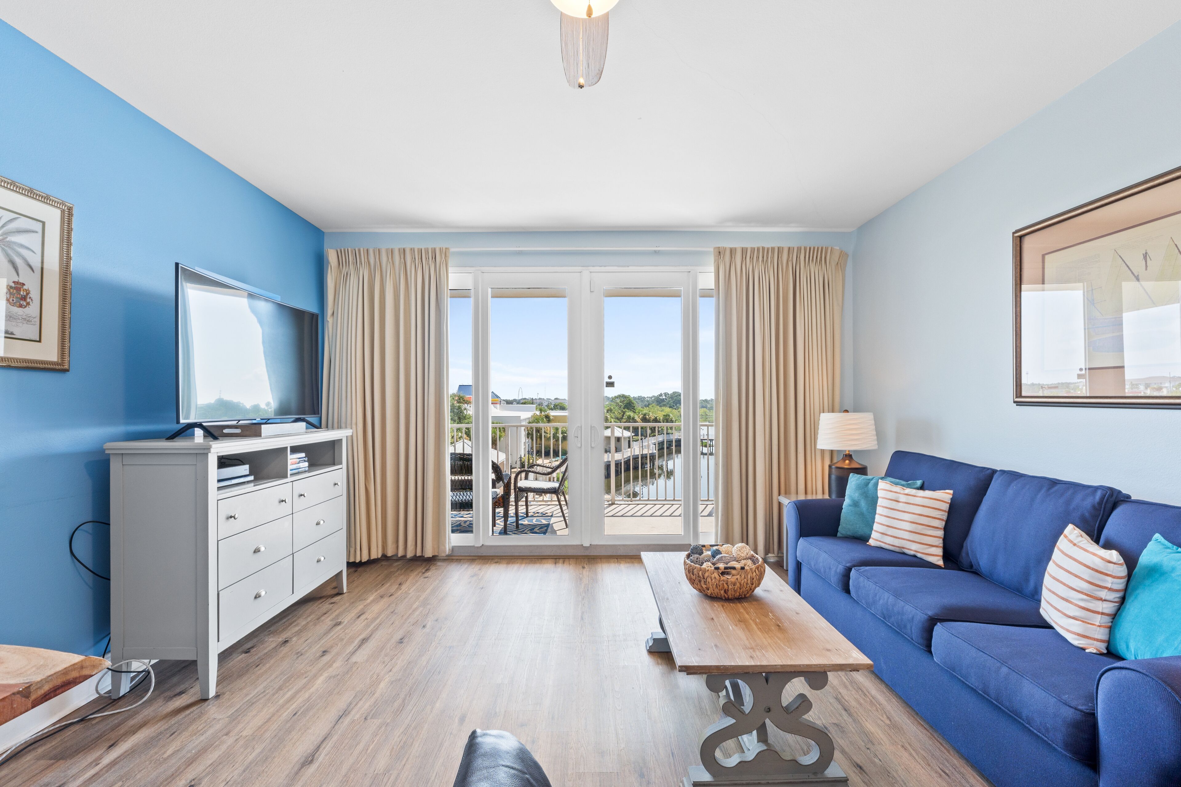 A modern living room with a blue sofa, a wooden coffee table, a white TV stand, and a balcony with outdoor furniture.