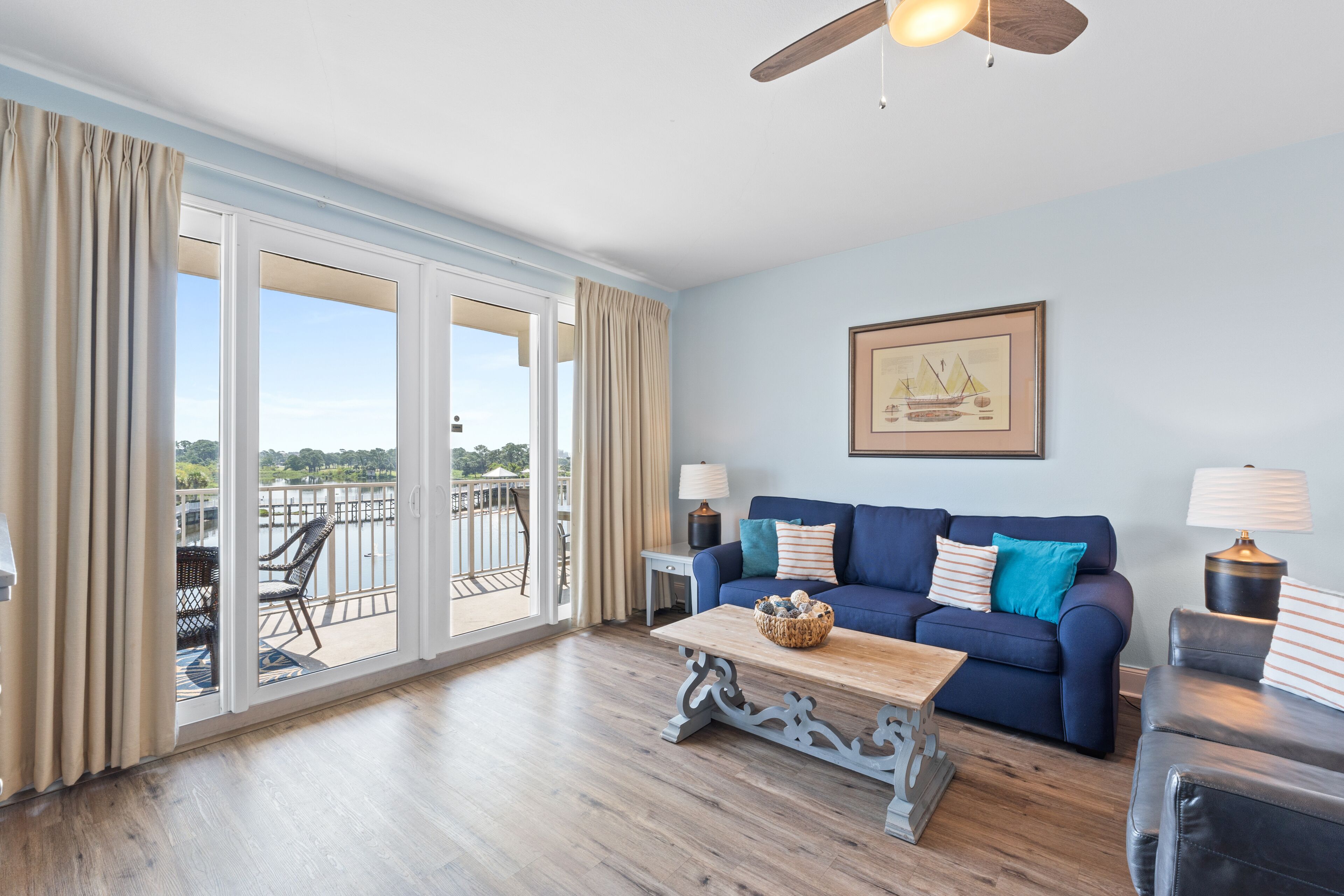 A living room with a blue sofa, a wooden coffee table, and a view of a balcony with outdoor furniture.