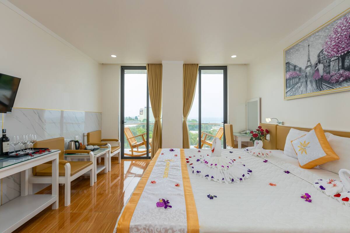 A hotel room with a bed, a desk with a computer, a chair, and a balcony with a view.
