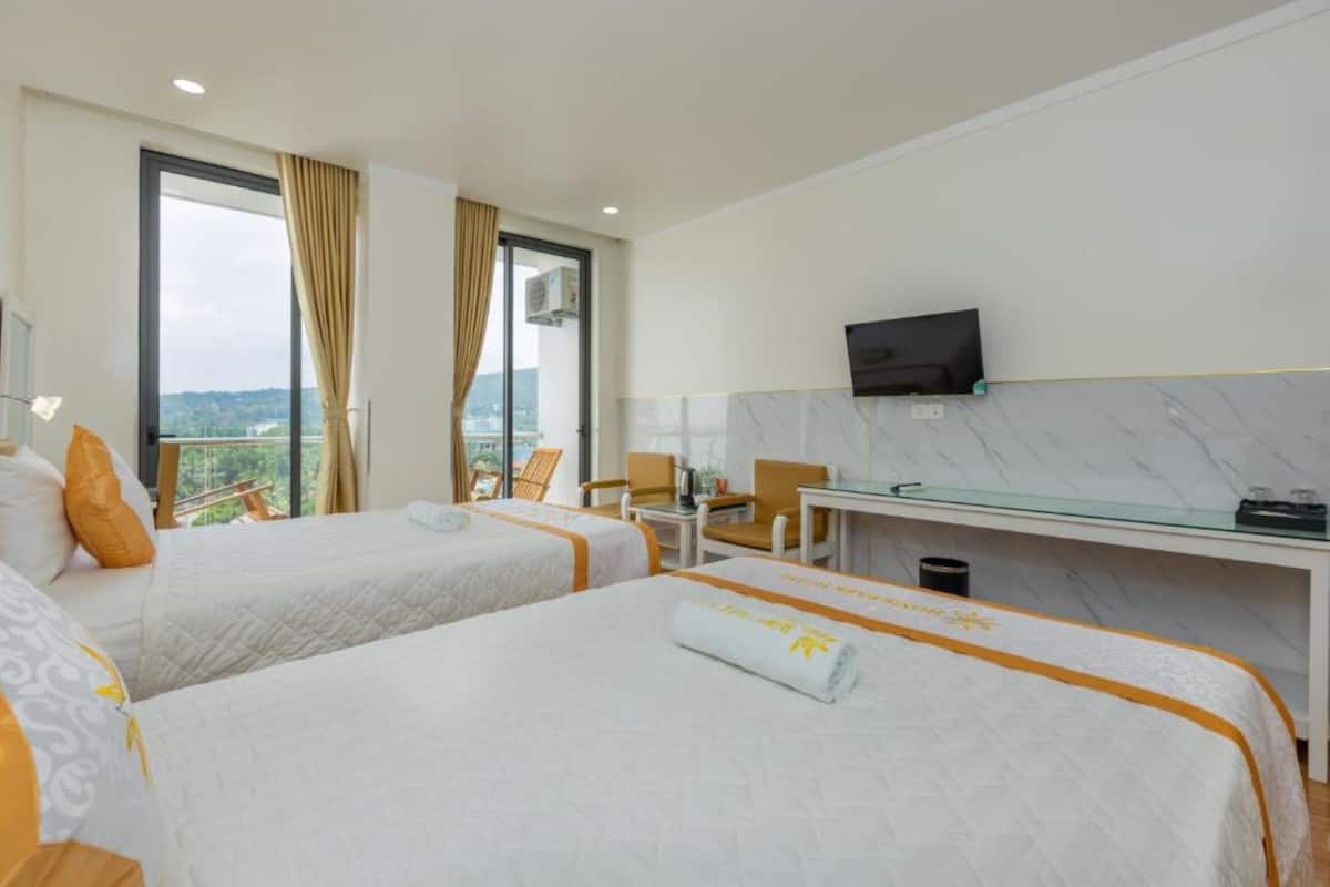 A hotel room with two beds, a desk, a TV, and a balcony with a view.