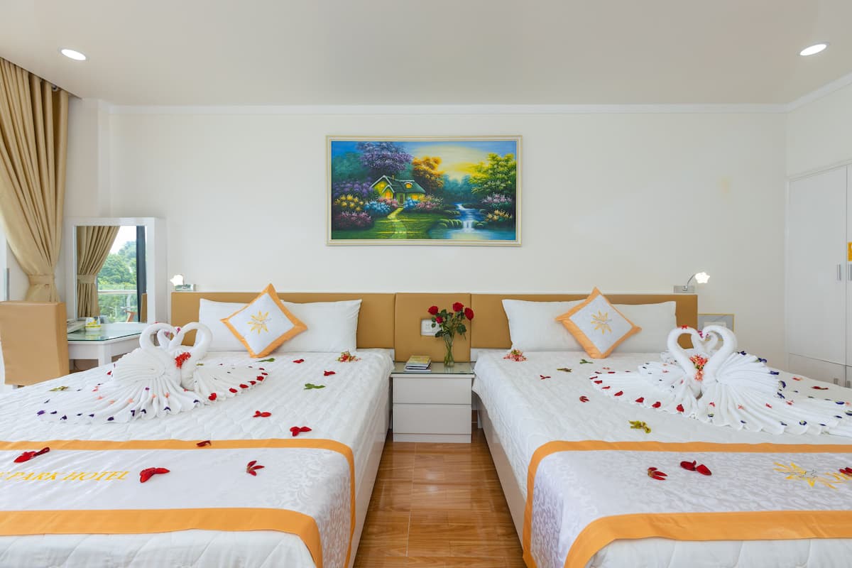 A hotel room with two beds, a painting of a landscape, and a nightstand with a vase of flowers.