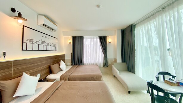 Habitación de hotel con dos camas, un sofá, una mesa de comedor y un gran ventanal con cortinas.
