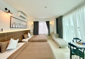 Ett hotellrum med två sängar, en soffa, ett matbord och ett stort fönster med gardiner.