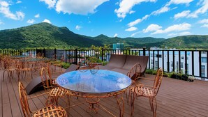 Terraza con mobiliario exterior, una mesa de vidrio y vistas a la montaña y al agua.