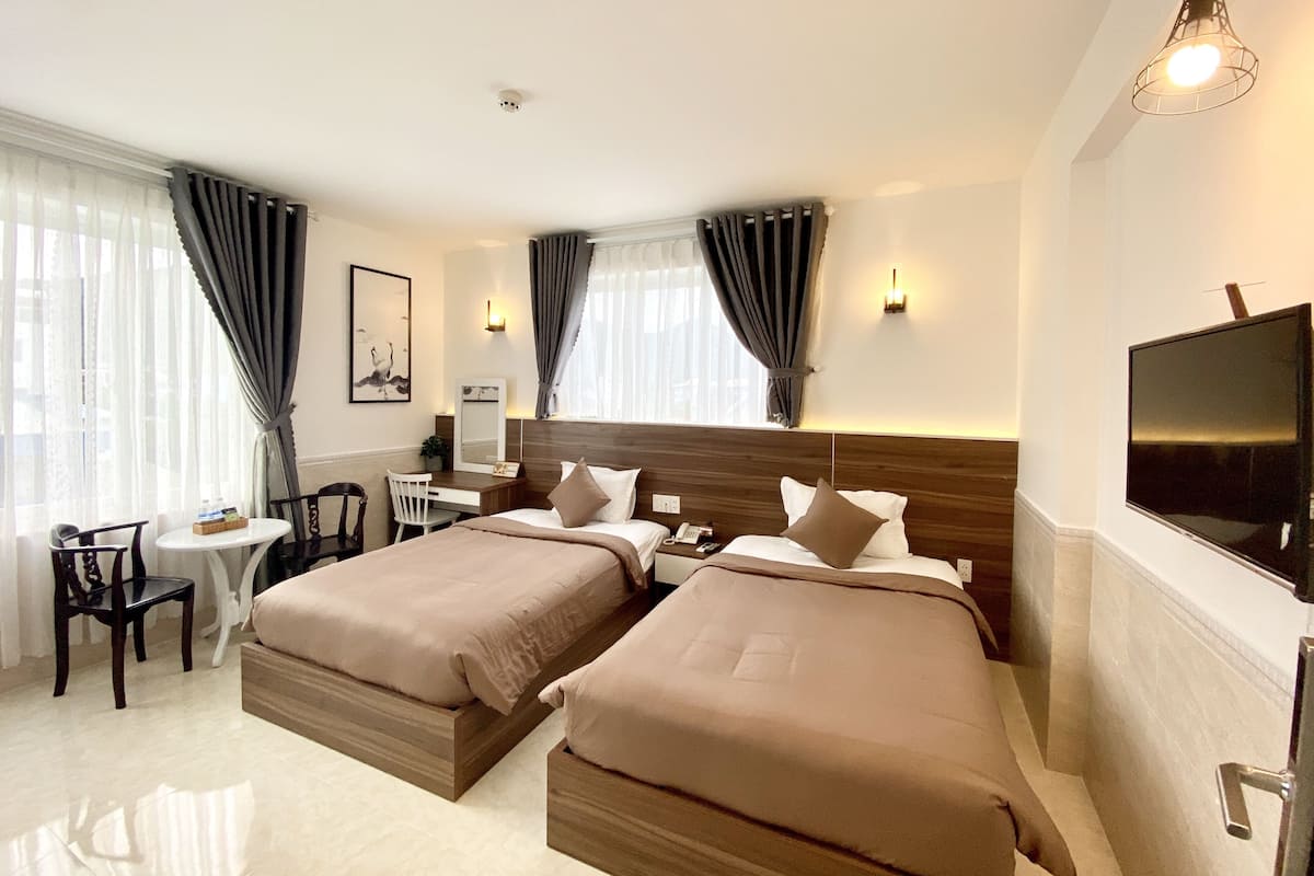 A hotel room with two beds, a desk, a chair, a TV, and a window with curtains.