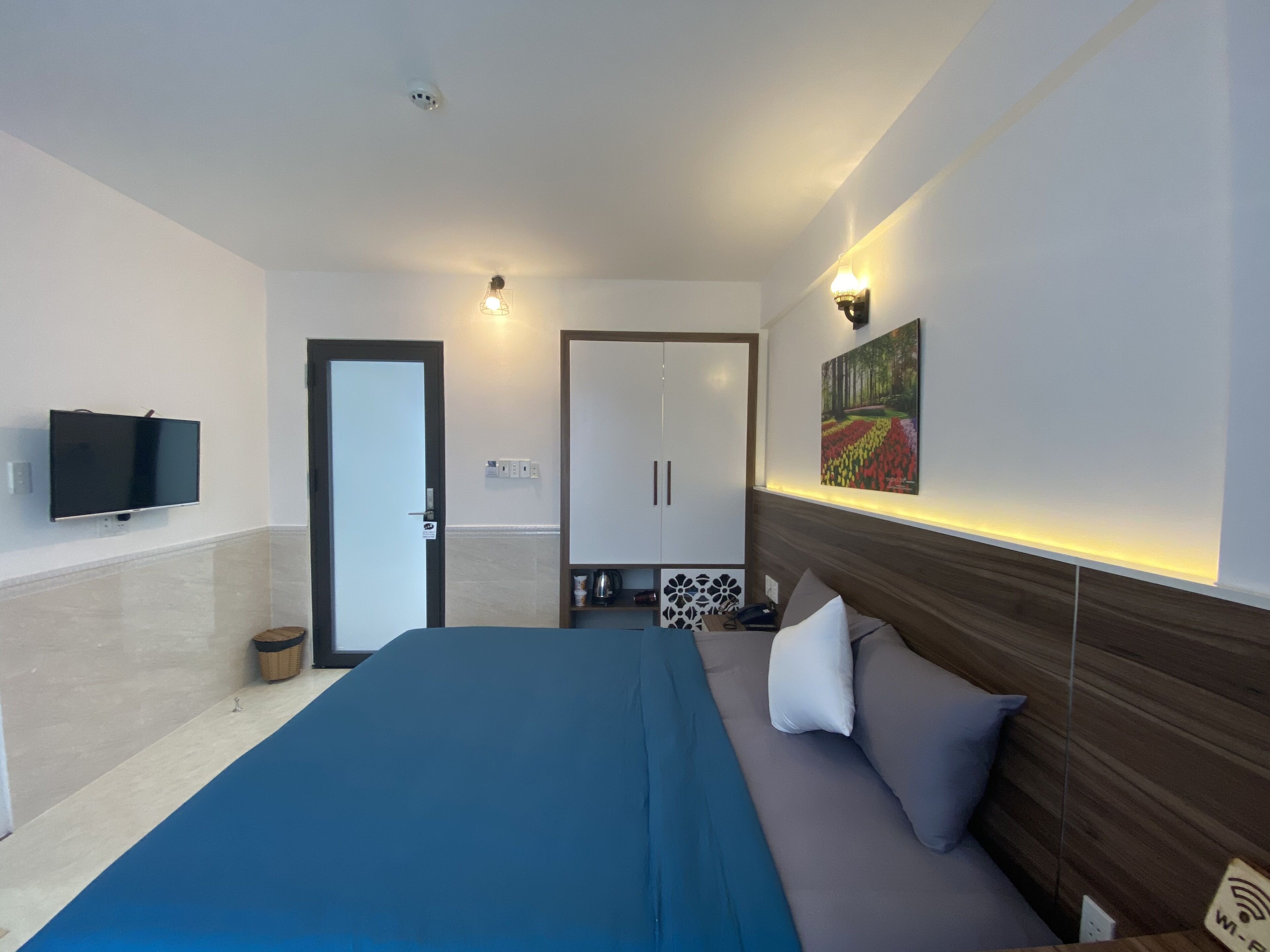 A modern hotel room with a large bed, a flat-screen TV, a wooden headboard, and a painting on the wall.