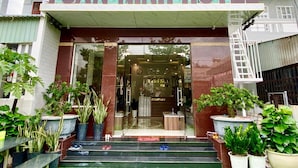 La entrada del Hotel Tuân Ninh, con un mostrador de recepción, puertas de cristal y plantas en macetas.