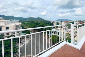 A balcony with a white railing overlooking a street with buildings and greenery.