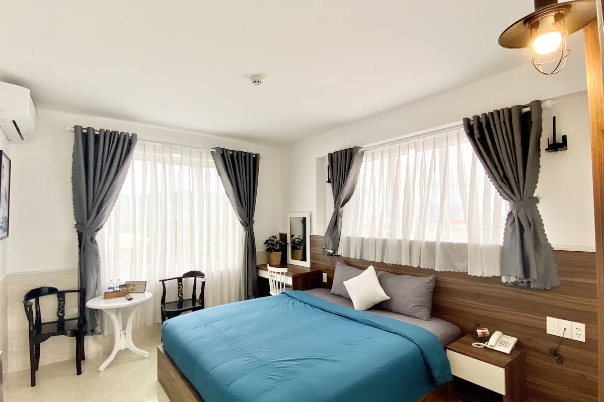 A bedroom with a bed, bedside table, chair, and a desk with a lamp.