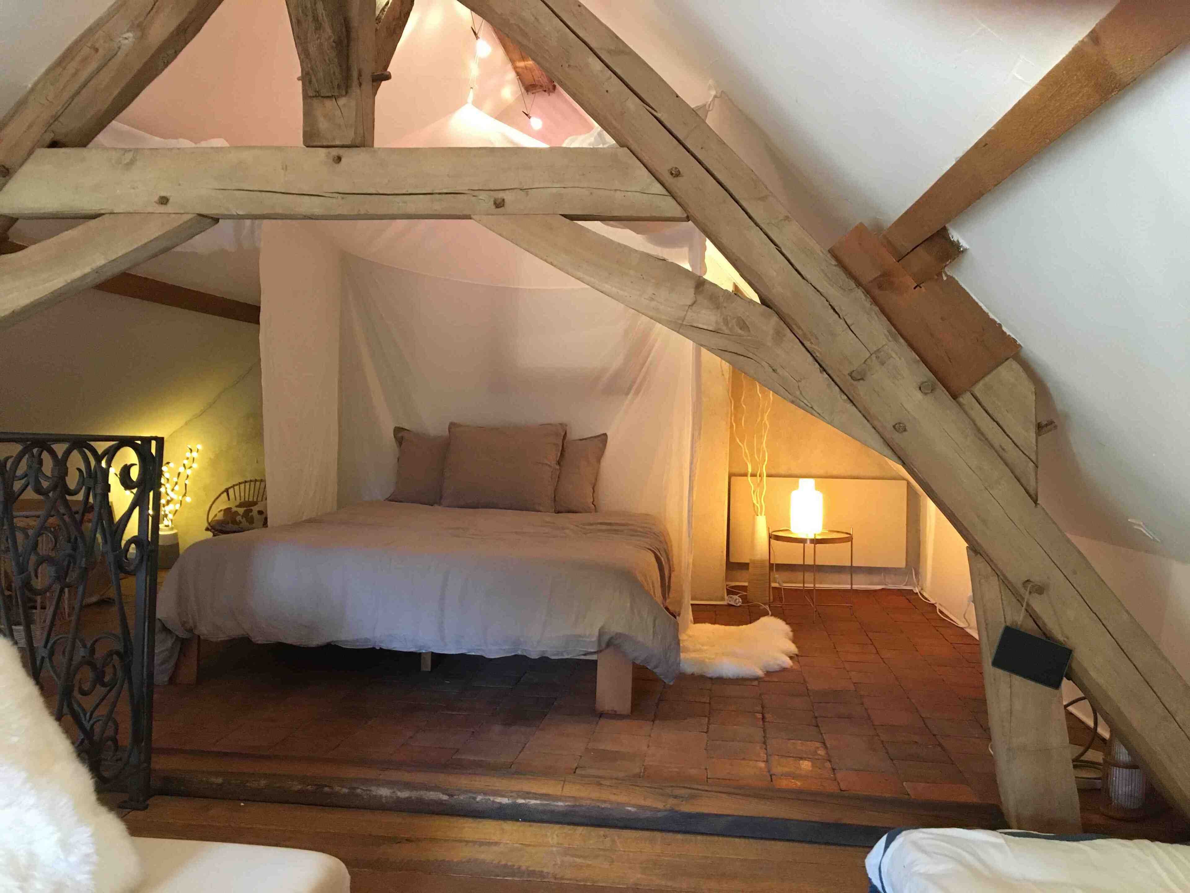 A cozy attic bedroom with a bed, a small table with a lamp, and a decorative metal gate.