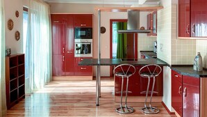 Een moderne keuken met rode kastjes, roestvrijstalen apparatuur en twee barkrukken.