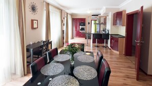 Een eethoek met een tafel gedekt voor vier personen, een vaas met bloemen, en een keuken op de achtergrond.