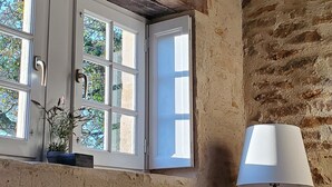 Une pièce aux murs en briques apparentes, une fenêtre avec des volets blancs, une chaise en métal et un lampadaire.