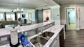 A modern kitchen with a marble countertop, stainless steel sink, and a refrigerator.