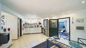 A modern kitchen with white cabinets, a stainless steel refrigerator, and a dining area with a glass table and chairs. - Finca Stemann - Casa Pascal (Guia de Isora)