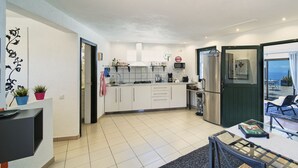 A modern kitchen with white cabinets, a stainless steel refrigerator, and a dining area with a glass table. - Finca Stemann - Casa Pascal (Guia de Isora)
