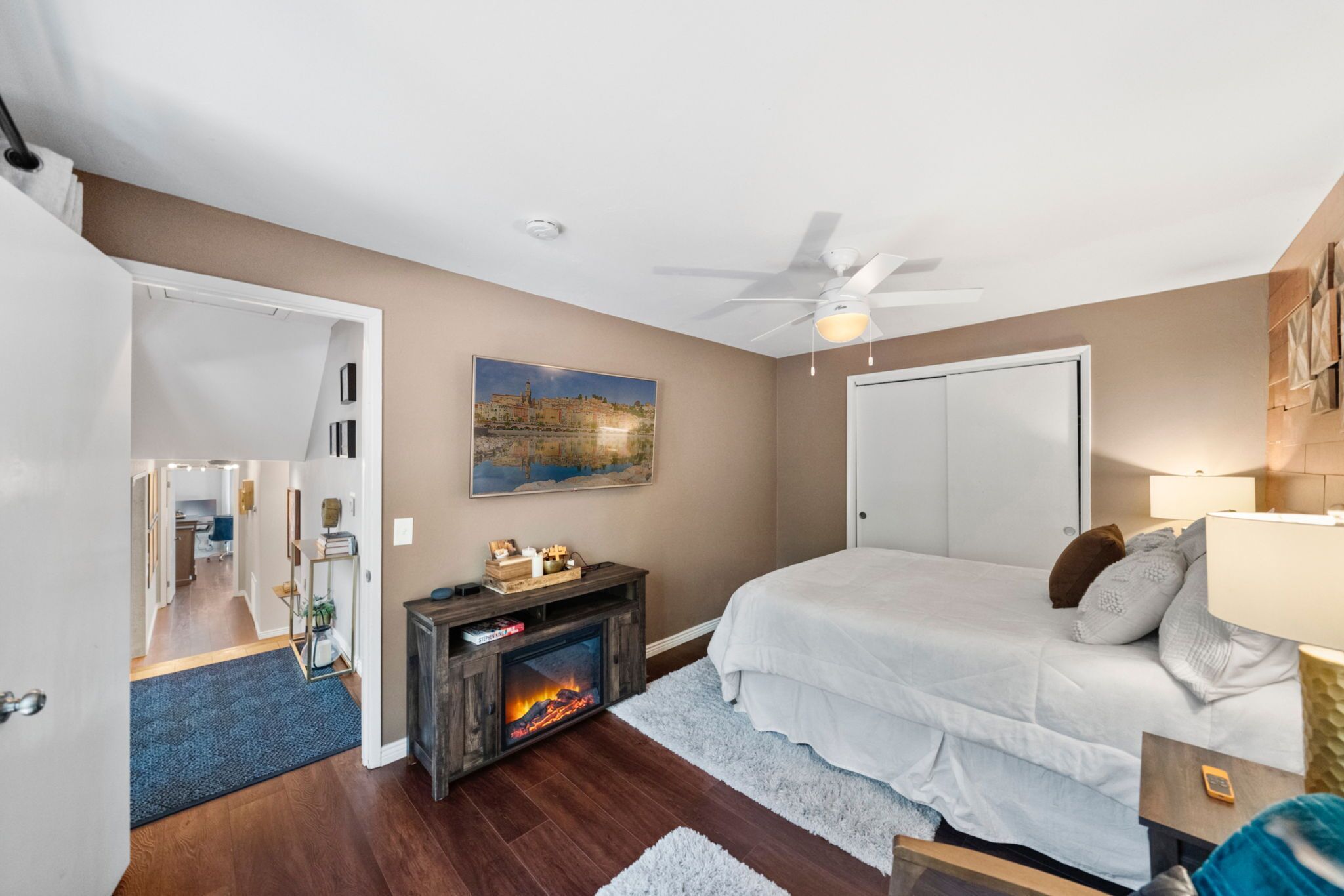 A bedroom with a fireplace, a bed, a ceiling fan, and a door.
