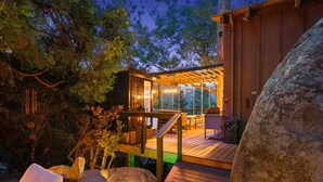A wooden deck with outdoor seating, surrounded by trees and a large rock. - Unique Modern Cabin w/spa, dry sauna (Idyllwild)
