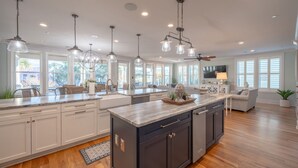 A spacious kitchen with a large island, pendant lighting, and a view of the outdoors. - 6-Bedroom Luxury House with Pool, Steps to Beach (Isle of Palms)