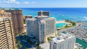 A high-rise hotel with multiple floors, a marina with boats, and a beach with palm trees. - @ Marbella Lane - Executive Suite | Steps to Beach (Honolulu)