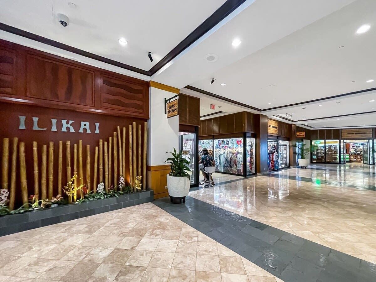 A spacious indoor area with a polished floor, a wooden wall with the name "ILIKAI" prominently displayed, and a potted plant in the center.