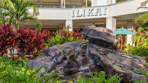 A hotel with a rock waterfall feature, lush greenery, and a sign reading "ILIKAI". - @ Marbella Lane - Executive Suite | Steps to Beach (Honolulu)