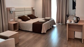 A hotel room with two beds, a desk with a kettle, and a television on the wall. - Hostal La Cigüeña (Sant Joan de Labritja)