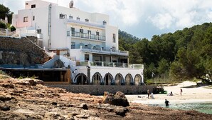 A coastal building with multiple balconies overlooking a beach. - Hostal La Cigüeña (Sant Joan de Labritja)