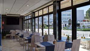 A restaurant with tables set for dining, large windows, and a view of the street. - Hostal La Cigüeña (Sant Joan de Labritja)