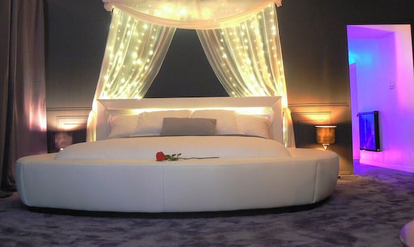 Une chambre à coucher moderne avec un grand lit, un baldaquin et une table de chevet avec une lampe.