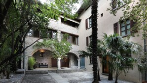 Um pátio com caminhos de pedra, palmeiras e um edifício com arcos e colunas.